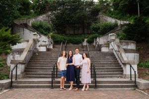 Portrait of family of 4 smiling, posing in park at base of stone steps - shot by Milwaukee family photographer Rachel Dickman.