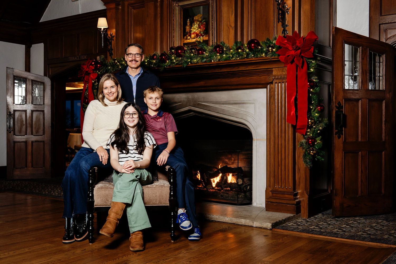A family snuggled together on a chair in front of a Christmas fireplace taken by Milwaukee family photographer Rachel Dickman.