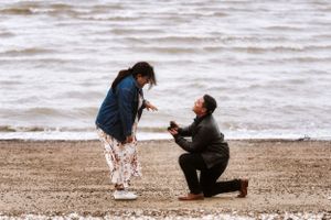 A romantic proposal scene unfolds on a misty beach with waves crashing in the background.