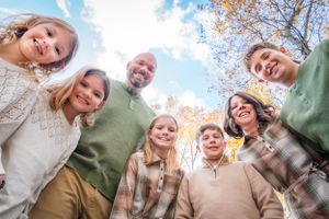 A group stands together in a circle formation looking down at the camera against a bright autumn sky.