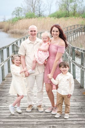 A family of five poses together on a wooden boardwalk surrounded by marsh grass on a sunny day.