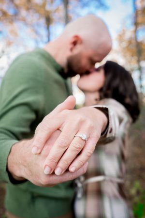 A close-up of an engagement ring with a couple sharing a romantic moment in the background.