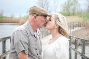 A romantic couple shares an intimate moment on a wooden boardwalk overlooking a marsh.