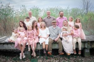 A large extended family group wearing pink and white poses together on a wooden deck by the marsh.