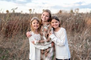 Three people in white sweaters pose together in a field of tall grass during autumn.