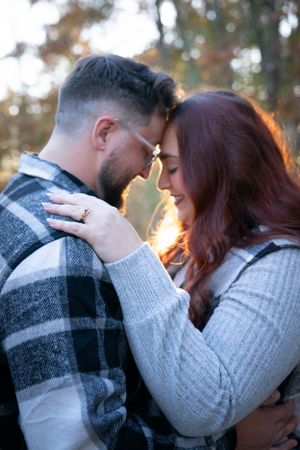 A tender embrace captured in soft lighting with autumn trees in the background.