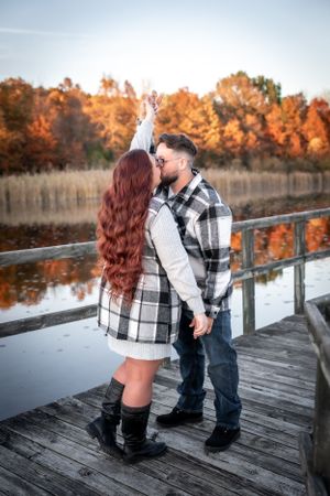 A romantic moment shared on a wooden dock with fall foliage in the background.