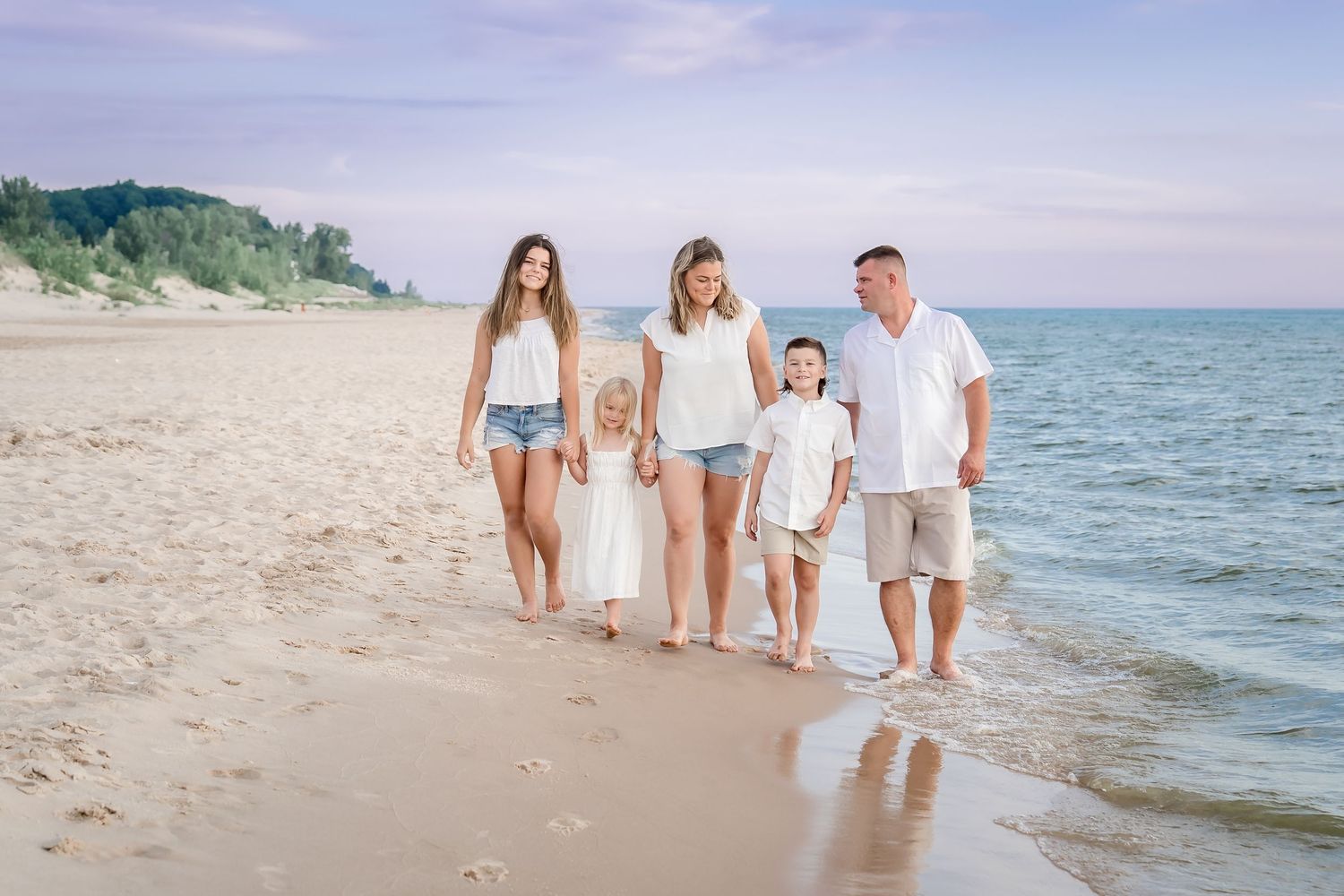 A family walks together along a sandy beach shoreline on a sunny summer day.
