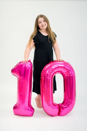 Studio portrait with large pink number 10 balloons and black dress for birthday celebration.