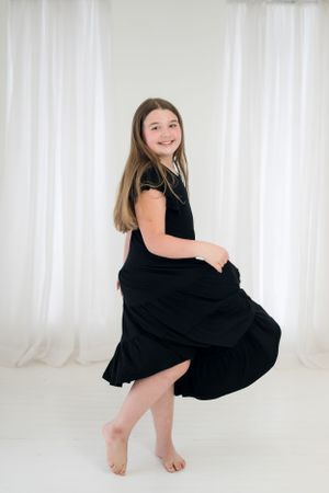 Young person in black dress twirling against white backdrop during studio photoshoot.