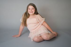 Studio portrait featuring person in peachy pink dress against grey background.