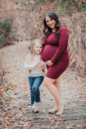 A mother and daughter play together in autumn leaves on a wooded path during a photo session.
