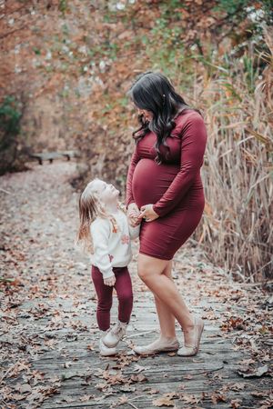 A touching autumn moment between parent and child in matching burgundy outfits playing among fallen leaves on a wooden path.