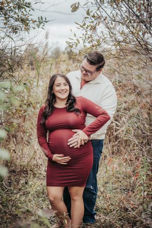 A couple poses together in a natural setting with fall foliage during a maternity photoshoot.