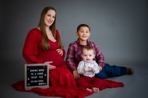 A maternity photo featuring a family of three on a red blanket with a letter board sign.