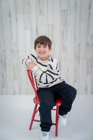 A child in a black and white outfit sits in a red chair against a white backdrop in a photo series.