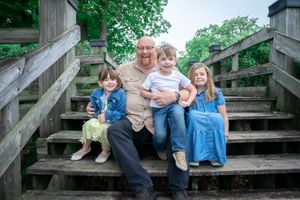 Family members sit together on wooden steps surrounded by lush green foliage in a candid outdoor portrait session.
