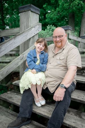 Two people share joyful expressions while sitting together on rustic wooden steps surrounded by lush greenery.