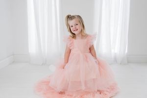A young child twirls in a fluffy peach-colored tulle dress against a bright white backdrop.