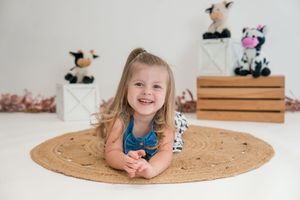Child lying on round jute rug in minimalist room with natural decor and white walls.