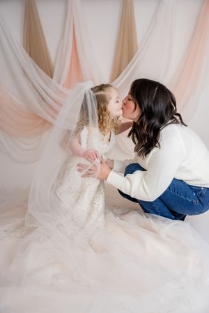 Two people in casual attire share a tender moment against a soft pink draped backdrop.