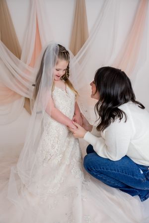 Two people in white and denim sit together against a romantic pink fabric backdrop.