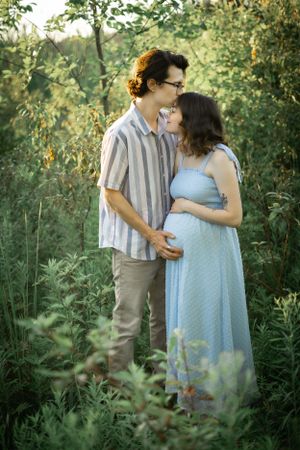 Romantic maternity photo of couple embracing in lush green garden setting.