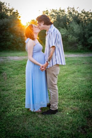 Expecting couple shares tender moment at sunset in pastoral setting.