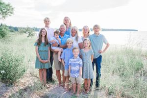 Family gathered together on a grassy lakeside wearing coordinated blue and white outfits for a summer portrait.