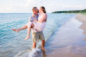 A romantic beach scene with someone carrying another in the shallow waters at sunset.