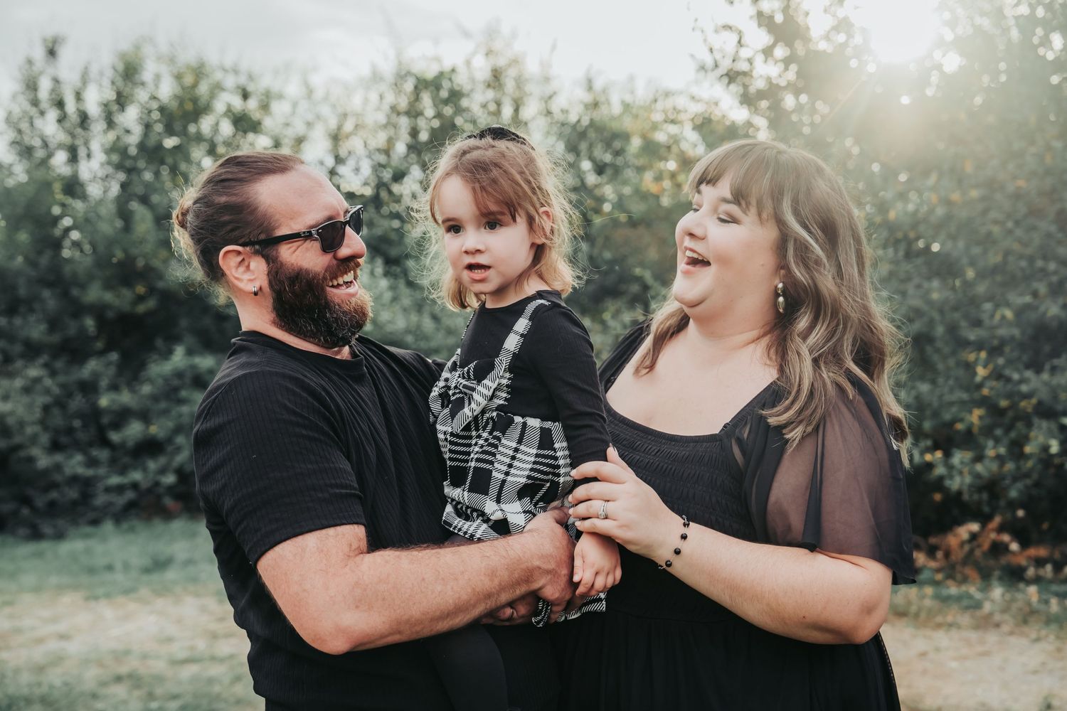 A family shares tender moments together in a sunlit outdoor setting during a lifestyle photography session.