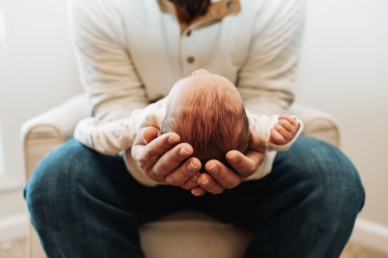 Father cradling newborn baby's head gently in hands during intimate newborn photography session.