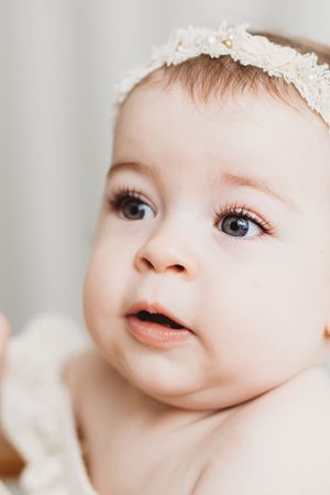 Close-up portrait of an adorable baby girl with big blue eyes wearing a delicate floral headband.