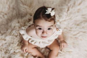 Baby in white lace dress photographed on cream textured backdrop.