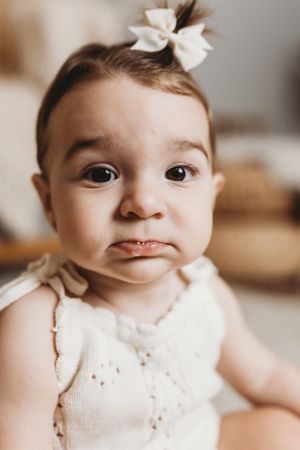 Close-up portrait of baby wearing white bow and lace outfit.