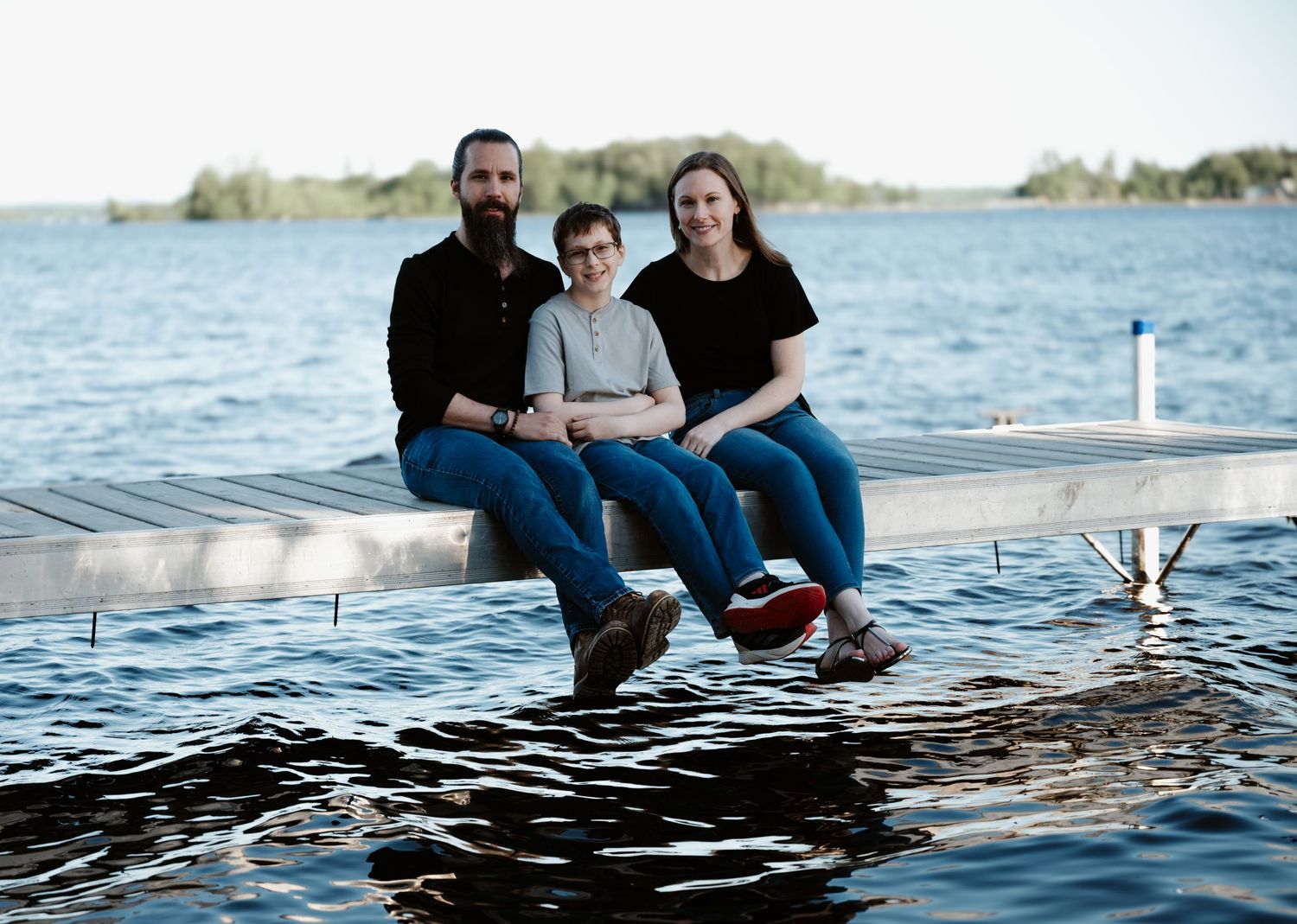 People relaxing on a dock with their feet dangling over calm lake waters at sunset.