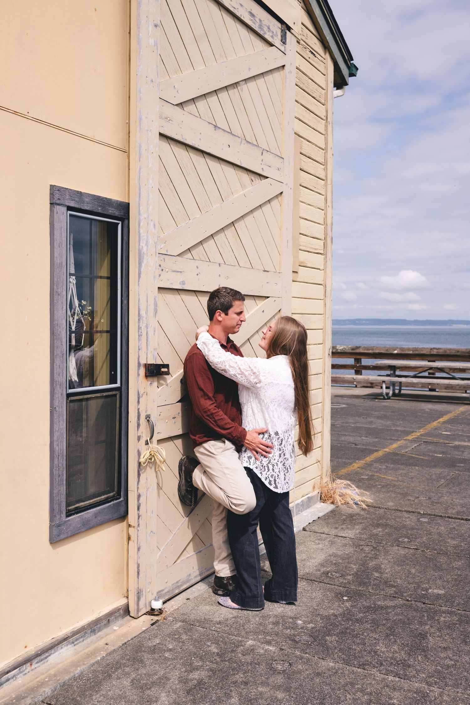 A romantic couple shares intimate moments against a sea shack wall with ocean views in the background.