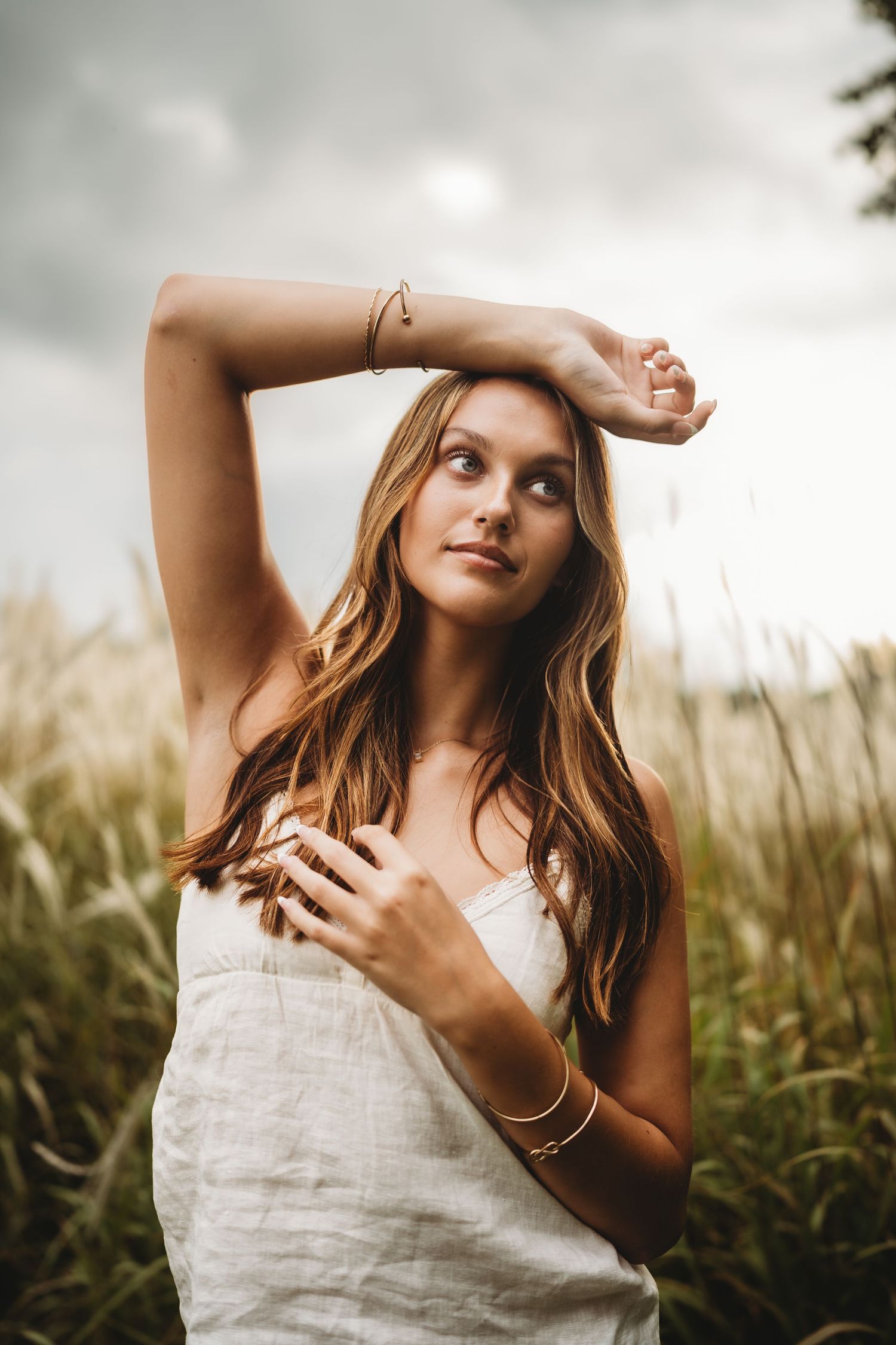Artistic outdoor portraits in a wheat field featuring someone in a white summer dress with flowing hair against cloudy skies.