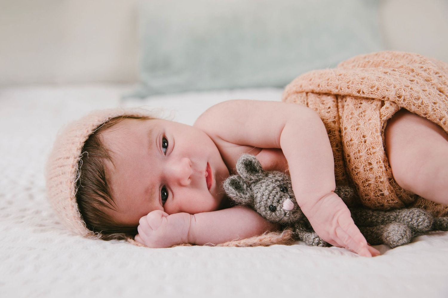 Baby in gray onesie lying on blanket with stuffed bunny toy.