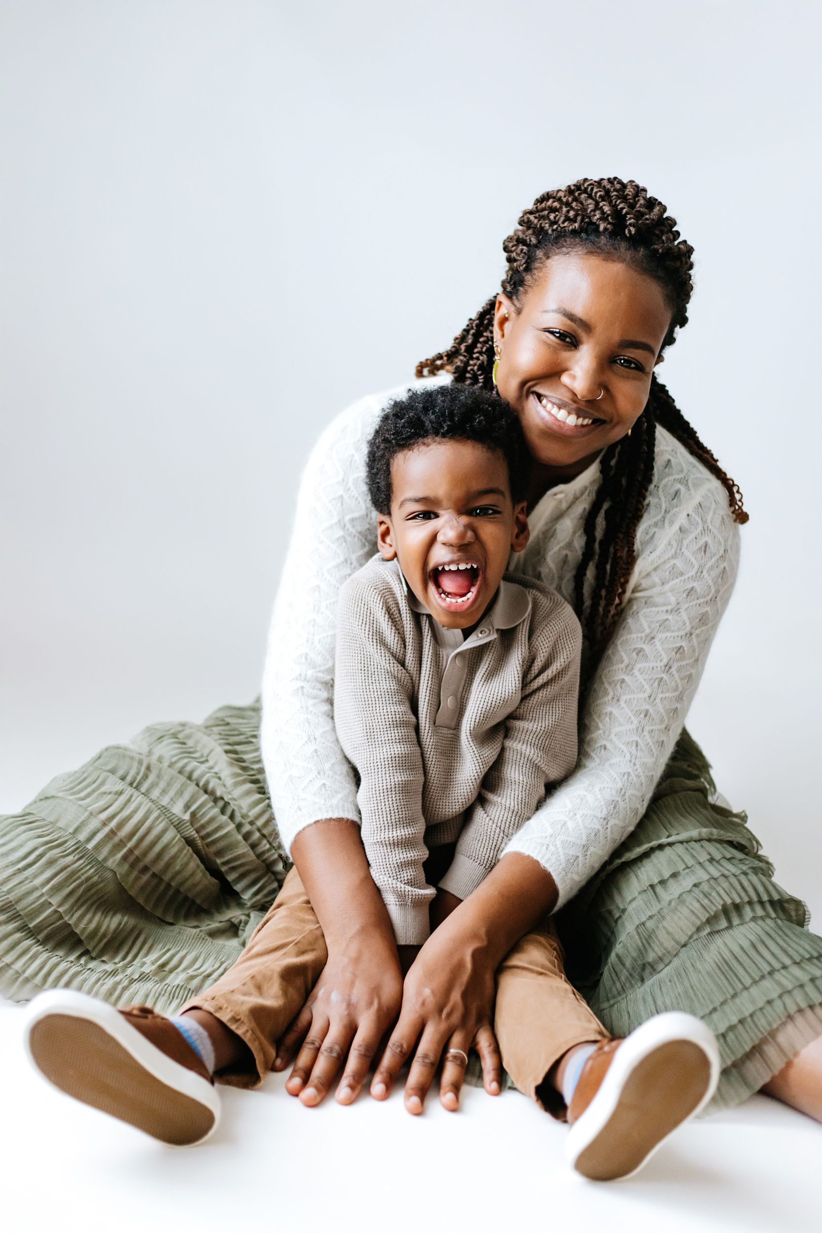 A joyful parent and child share a candid laughing moment while sitting together on a white backdrop.