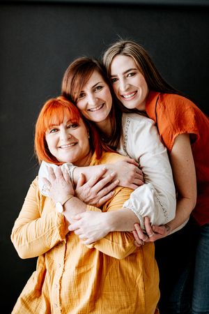 Three generations embrace in a joyful group hug, wearing vibrant orange and white clothing against a dark background.