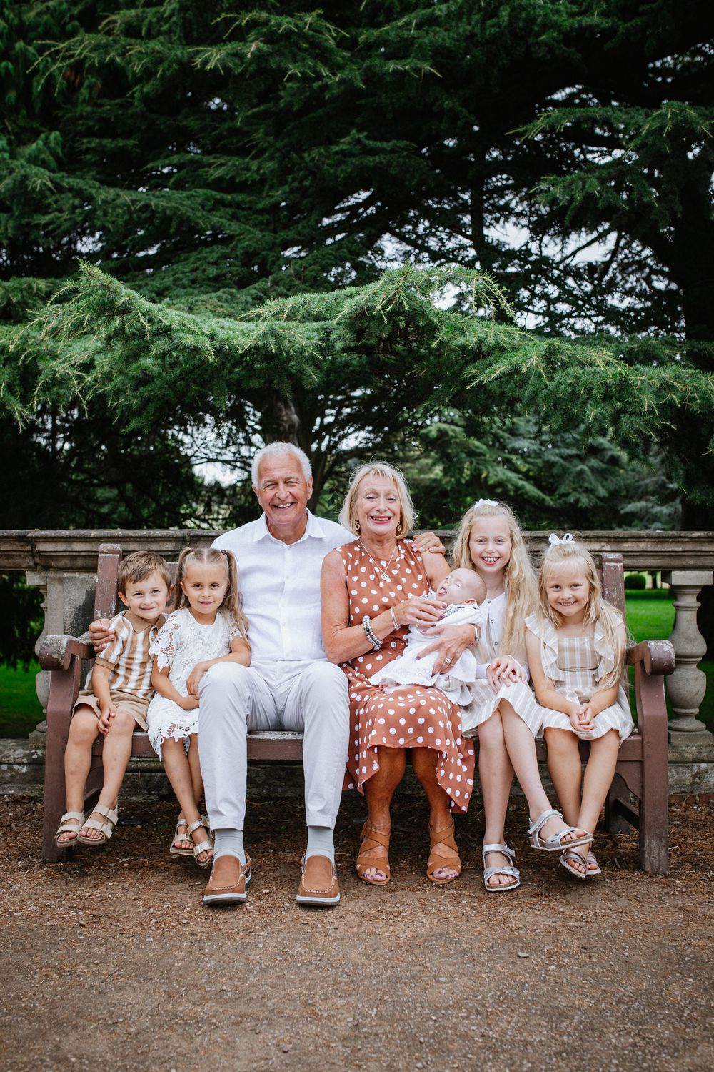 Family photoshoot at Wollaton hall Nottingham on stone bench in garden setting with evergreen trees in background.