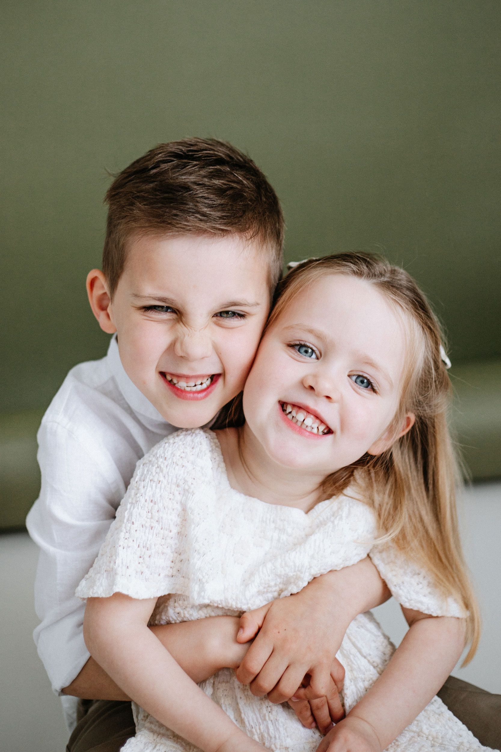 A series of five connected photos showing two young siblings embracing and laughing together against a green background.