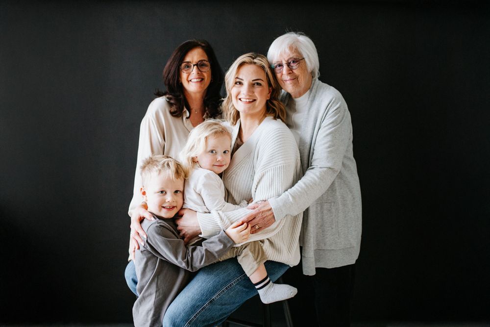 Multi-generational family wearing white and denim poses together against a dark background in studio portrait.