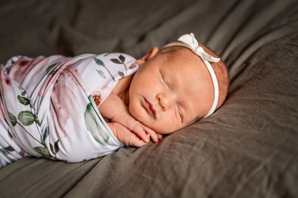 Sleeping baby wearing floral print outfit lies on white bedding in series of connected photos.