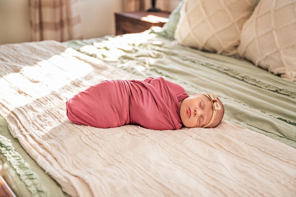A series of images showing a sleeping newborn baby wearing red clothing on a white bed.