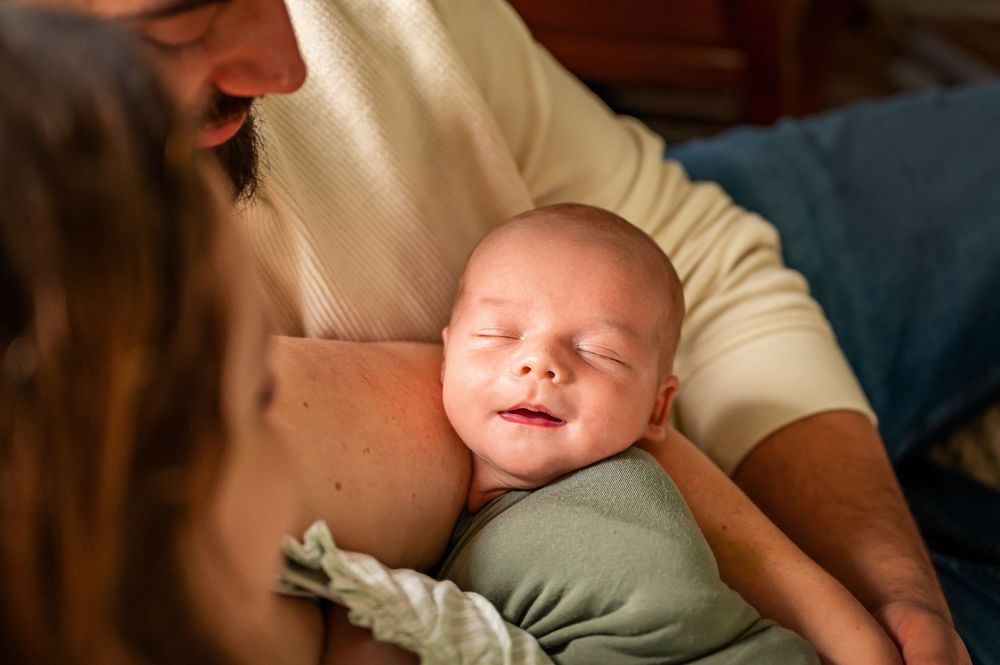 A newborn baby sleeps peacefully while being cradled in someone's arms.