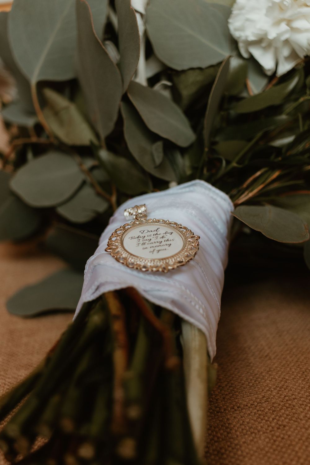 Bridal bouquet with white flowers, eucalyptus, and decorative gold charm detail.