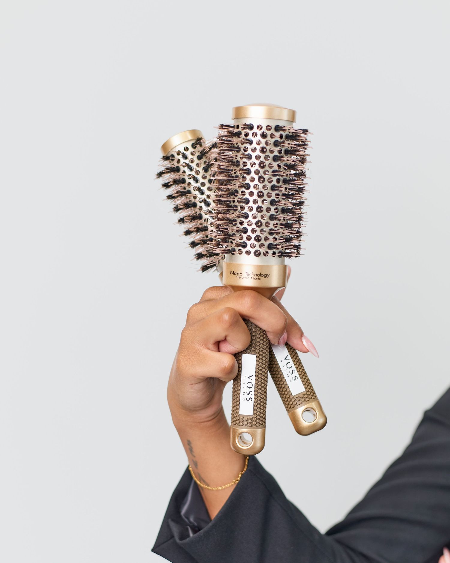 Hand holding two gold-colored round styling brushes against white background.