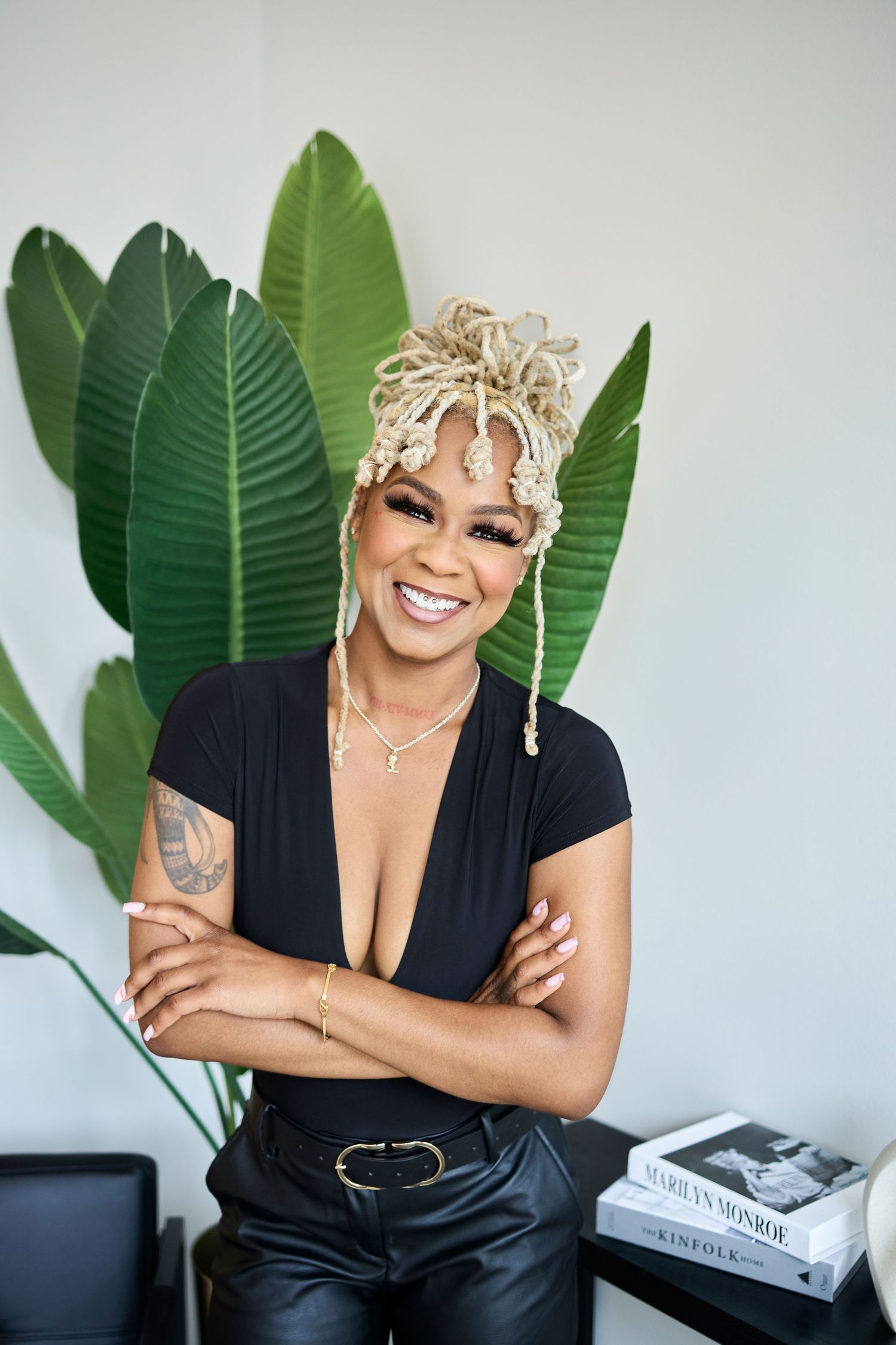 Stylish woman posing against tropical leaves wearing black top with unique blonde braided hairstyle.